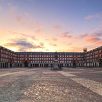 Madrid, Spain - April 30, 2018: Overview of Plaza Mayor (English Main Square) during sunrise.
The Plaza Mayor was first built (1580–1619) during Philip III's reign and is a central plaza in the city of Madrid; is rectangular in shape and is surrounded by three-story residential buildings having 237 balconies facing the Plaza. It has a total of nine entrance ways. The Casa de la Panadería (Bakery House), serving municipal and cultural functions, dominates the Plaza Mayor.
There is a bronze statue of King Philip III at the center of the square, created in 1616 by Jean Boulogne and Pietro Tacca.
The Plaza Mayor represents the work of Juan de Villanueva, one of Spain’s most famous neoclassical architects, who managed to reconstruct it after several fires suffered over the years.